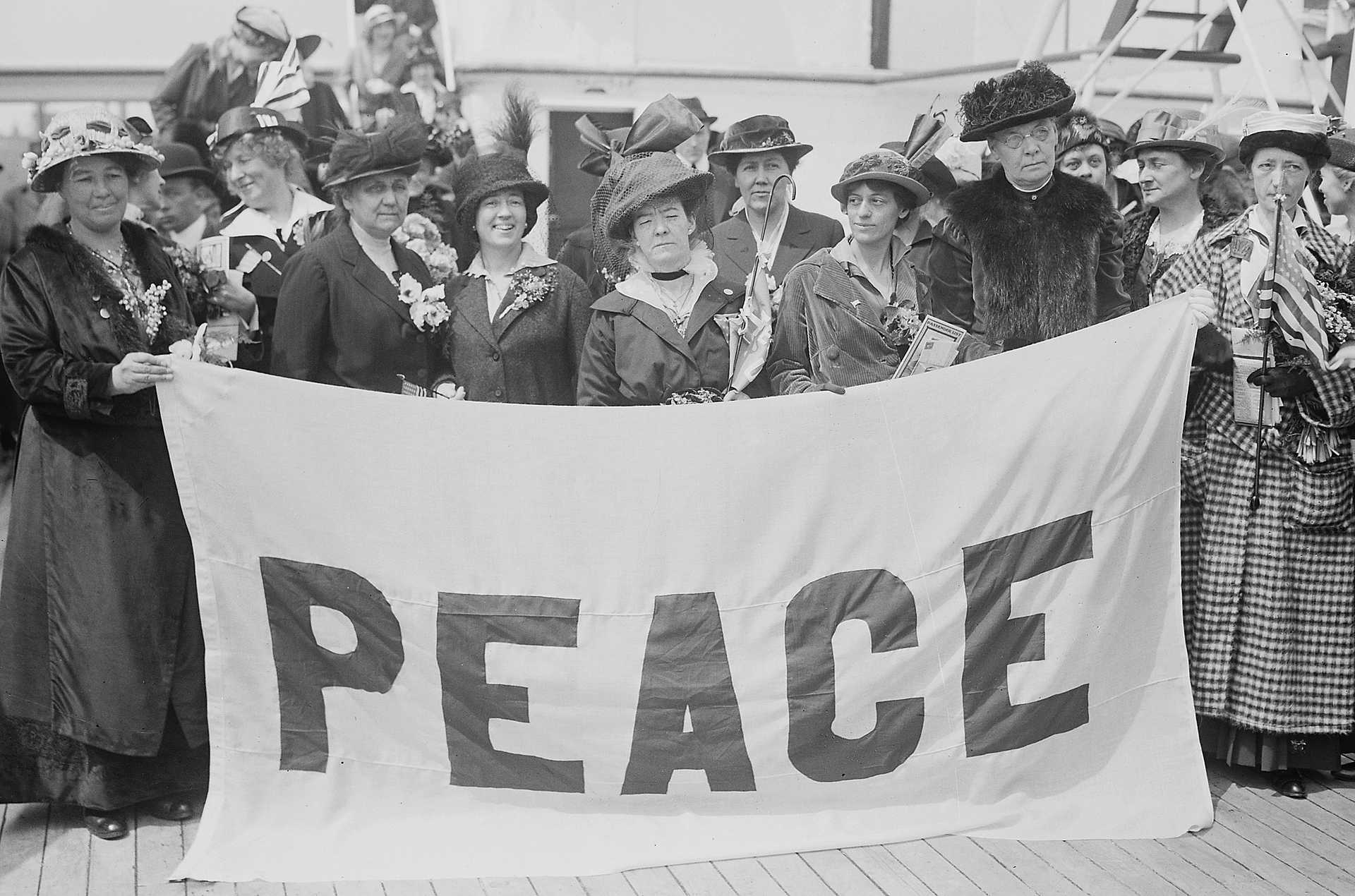 Black and white photograph of women holding a large white banner reading: PEACE